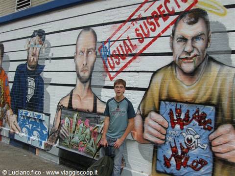 Boy standing in front of mural with painted faces on striped white wall