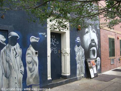 Mural of male portraits on blue wall beside a doorway, tree branches above