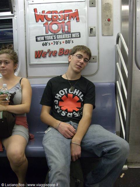 Young man asleep in Red Hot Chili Peppers shirt on a blue subway seat