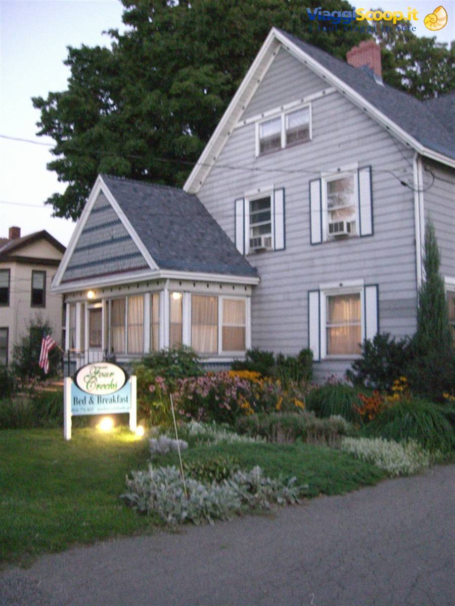 Gray wooden house with porch and bed and breakfast sign among flowers
