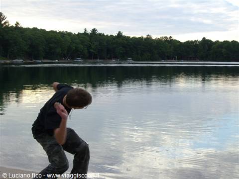 Boy in black t-shirt skipping a stone across a forest-fringed lake