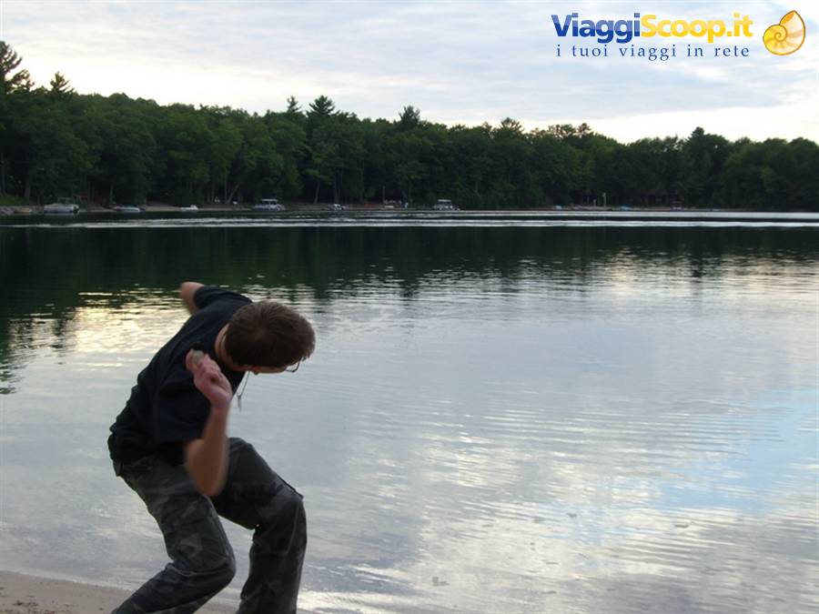 Boy in black t-shirt skipping a stone across a forest-fringed lake