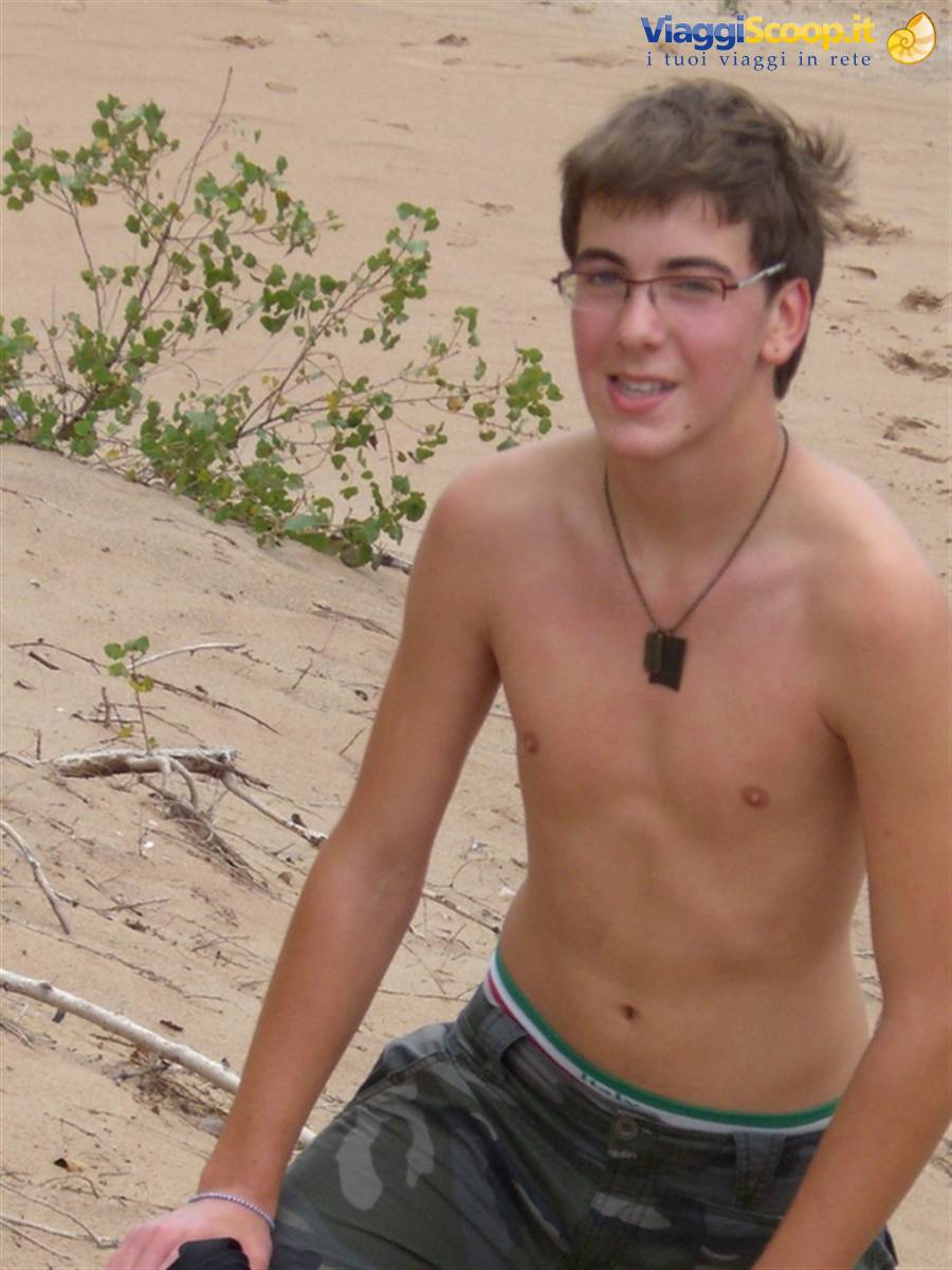 Shirtless boy with glasses and black pendant, sitting on sand