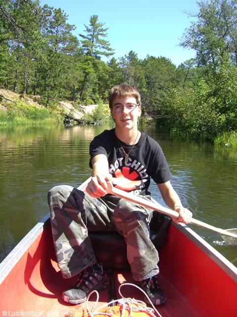 Boy with glasses paddling a red canoe on a river among pine trees