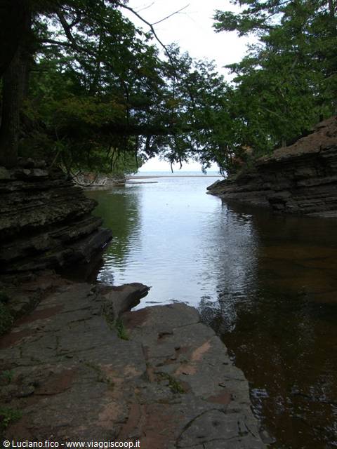 Rocky creek flows between layered sandstone and pines into Lake Superior