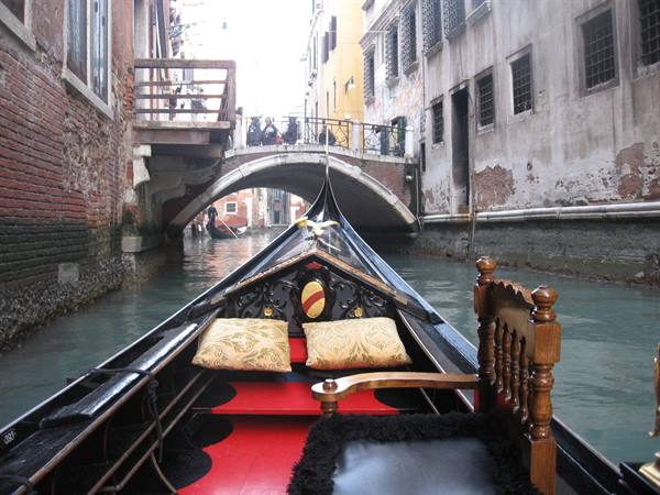Black gondola with golden cushions gliding under a bridge in Venice
