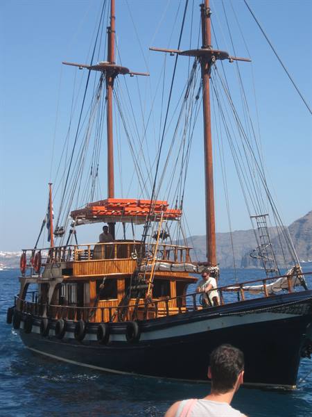 Wooden two-masted boat with black hull anchored off Santorini's volcanic cliffs