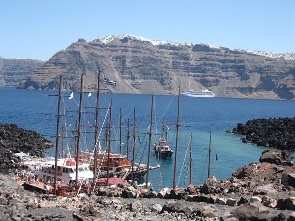 Boat moored in Santorini caldera, volcanic cliffs and cruise ship beyond