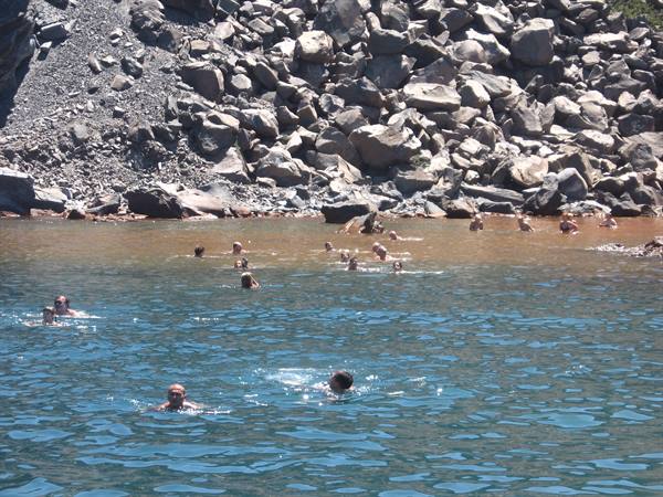 Swimmers in turquoise water below a grey boulder slope