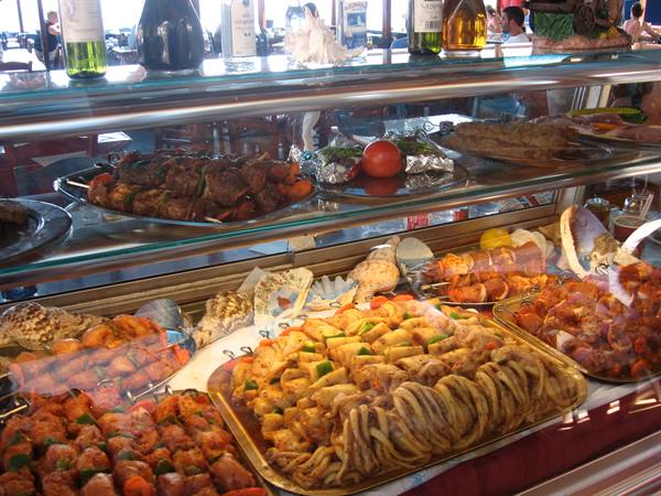 Food counter with skewers, shellfish and bottles behind reflective glass