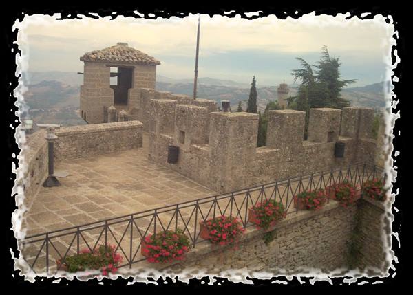 Crenellated walls of Guaita in San Marino, red geraniums along the railing