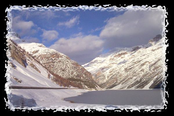 Frozen lake between snow-covered mountains, long gallery along the road