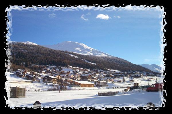 Snowy alpine village with wooden chalets beneath a snow-capped mountain, Livigno