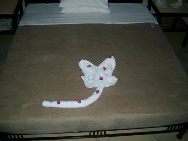 Towel folded into a flower shape with pink petals on the hotel bed