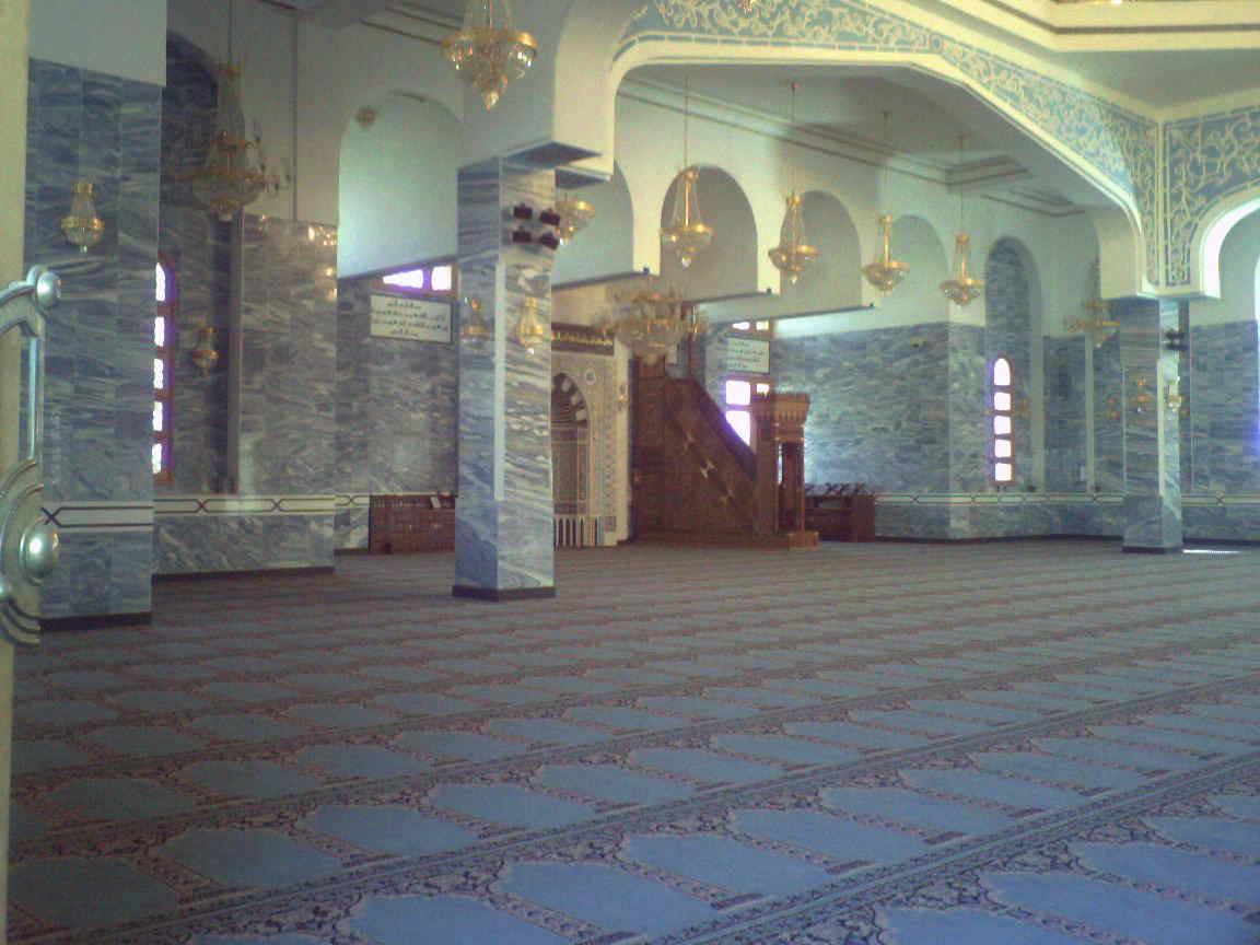 Mosque interior with blue carpet, grey marble columns and golden chandeliers