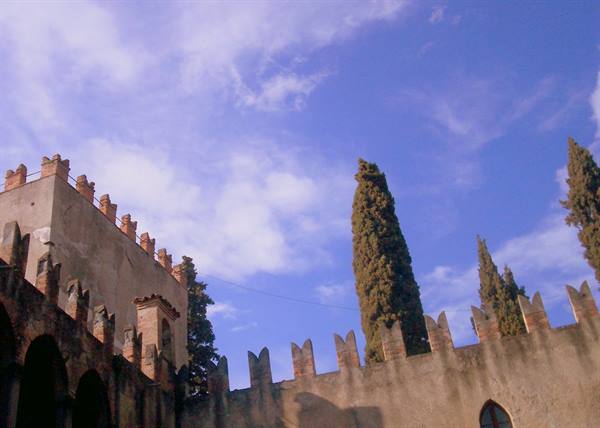 Crenellated stone walls with tall cypresses against a blue cloudy sky