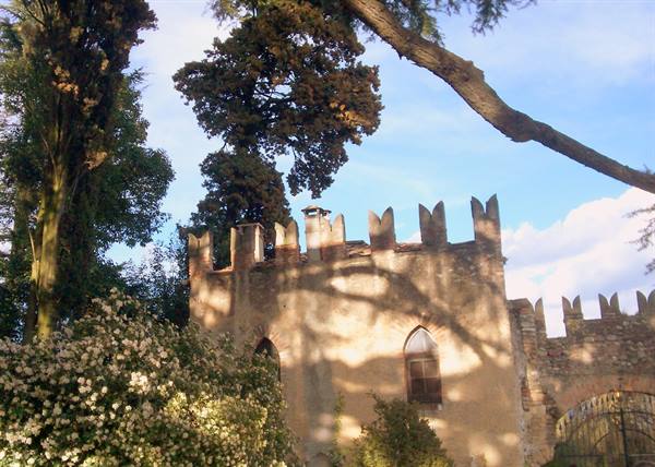 Crenellated stone castle walls among trees and white flowers, sunlight