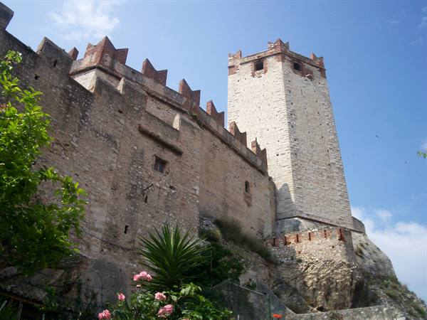 Crenellated tower and stone walls of Malcesine castle against blue sky
