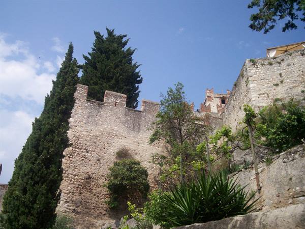 Stone castle walls at Malcesine, cypresses and agaves under sunny sky