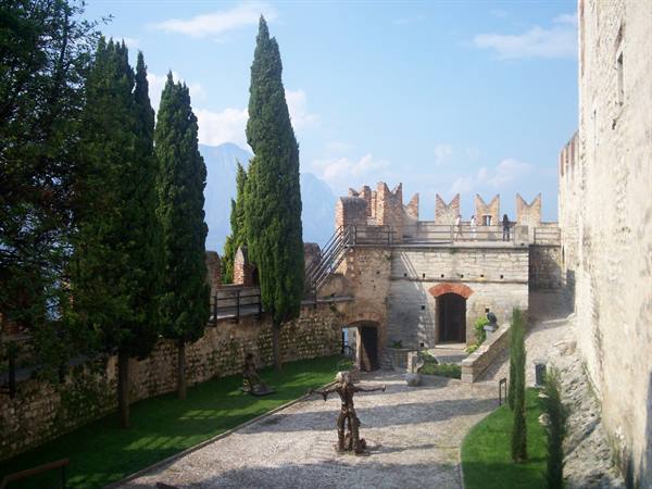 Courtyard of Malcesine Castle with crenellated walls, cypresses and statue