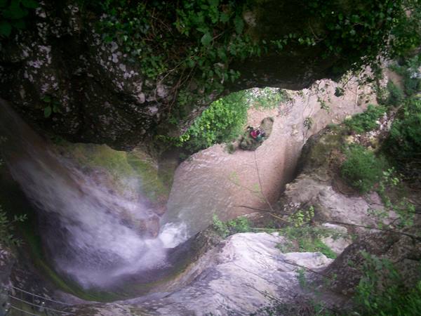 Waterfall over mossy rocks seen from above, murky stream below