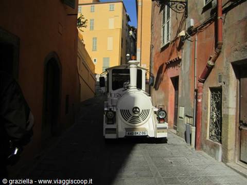 white tourist train climbing a narrow alley between colorful old buildings
