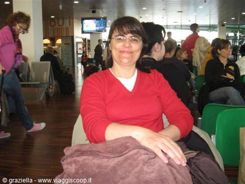 Smiling woman in red sweater sitting in a crowded waiting area