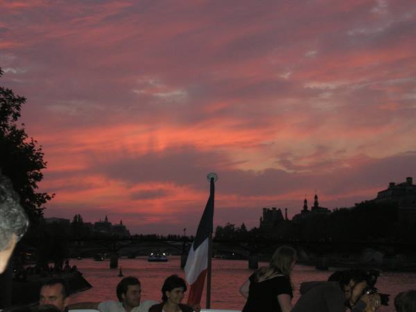 Tourists on a Seine boat in Paris, pink glowing sky and French flag