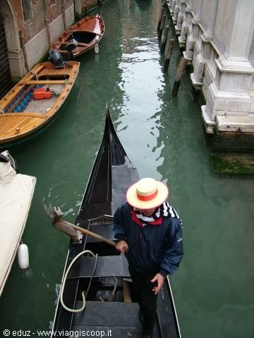 Gondolier in straw hat rows through Venice canal between wooden boats