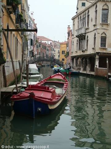 Red boat moored along a Venice canal with bridge and old buildings