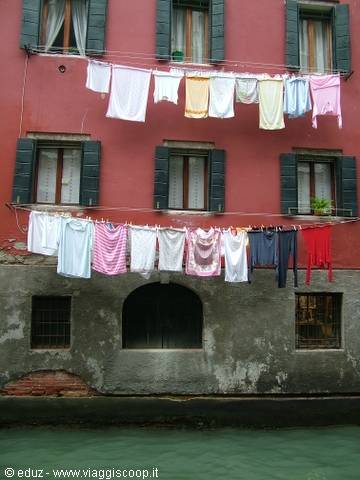 Laundry hanging on lines outside a red house along a Venice canal