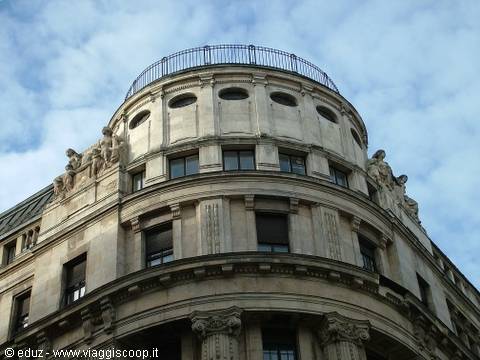 Curved stone facade with statues and balustraded rooftop terrace, cloudy sky