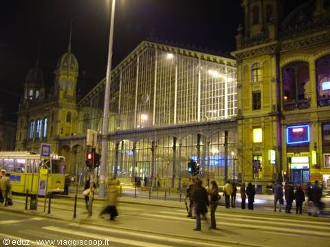 Budapest Nyugati station at night, glass and steel facade, yellow tram, pedestrians