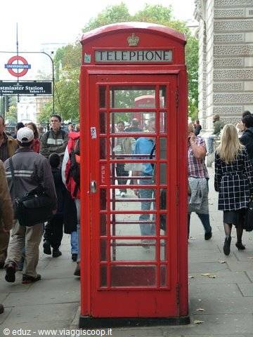 Red telephone box in London among pedestrians near the station