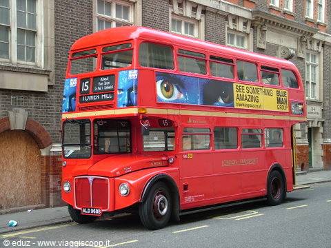 Red double-decker Routemaster on route 15 to Tower Hill by brick buildings