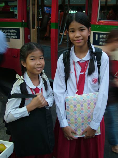 Two schoolgirls in white and red uniforms in front of a city bus