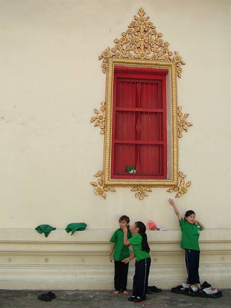 Schoolgirls in green uniforms play beneath a red window with golden ornaments