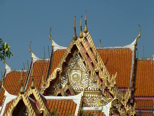 Golden spires and orange tiled roofs of a Thai temple against blue sky