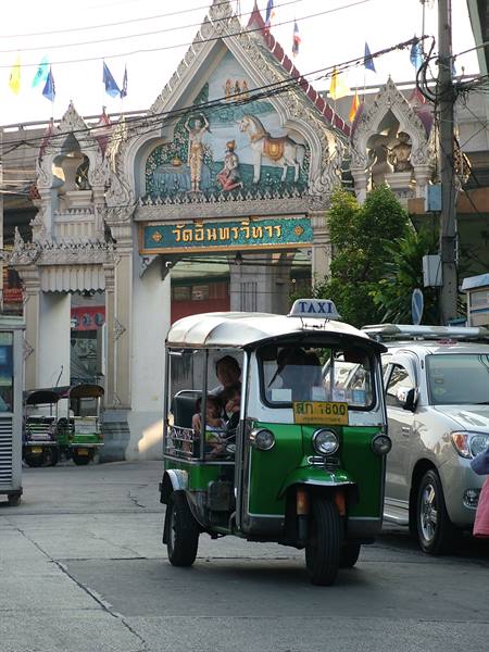 Green and grey tuk-tuk in front of the ornate gate of Wat Suthat Thepwararam, Bangkok