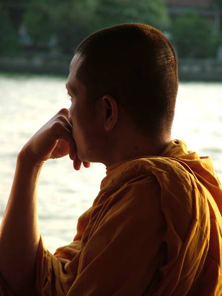 A pensive Buddhist monk in orange robe beside a river