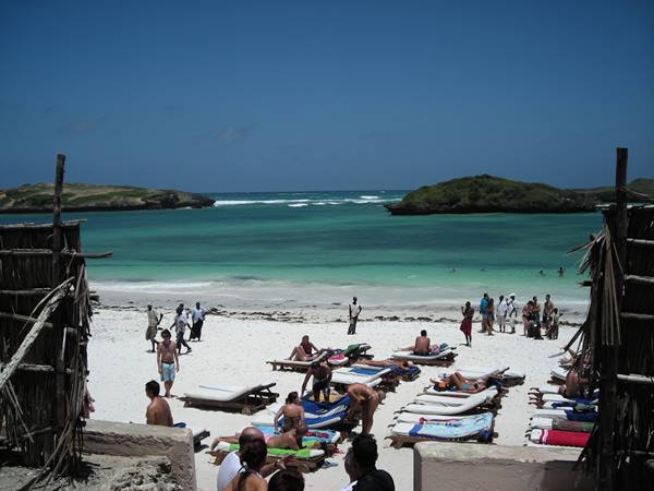 Tourists on sun loungers, white sand beach, turquoise bay with green islets