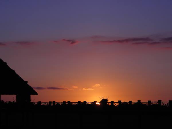 Thatched roof and wooden fence silhouetted against the sinking sun