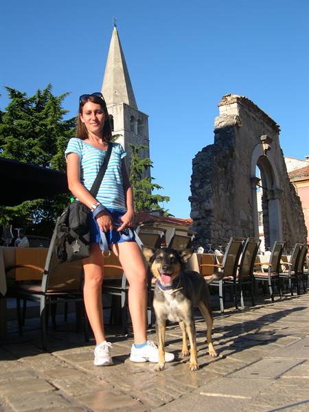 Woman with dog beside outdoor café tables and Roman ruins in Zadar
