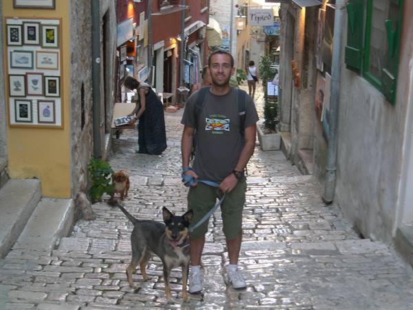 Man with backpack and leashed dog on cobblestone alley in Rovinj