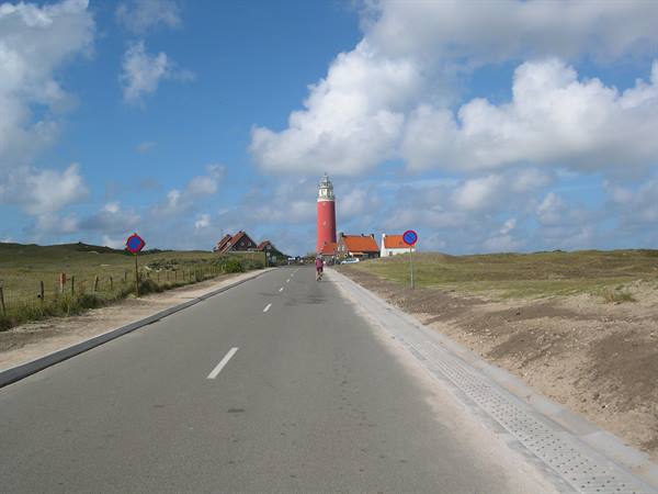 Road with cyclist toward the red Texel lighthouse, tiled-roof houses