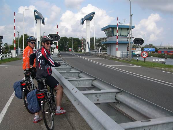 Two cyclists with loaded bikes stop on a bascule bridge near the control tower