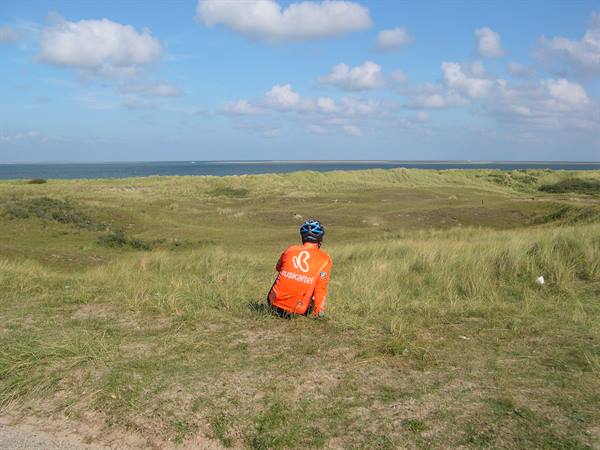 Cyclist in orange jersey sitting on grassy dunes facing the sea