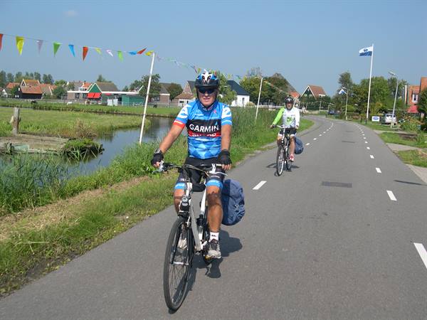 Cyclists riding on paved path beside canal and traditional Dutch houses