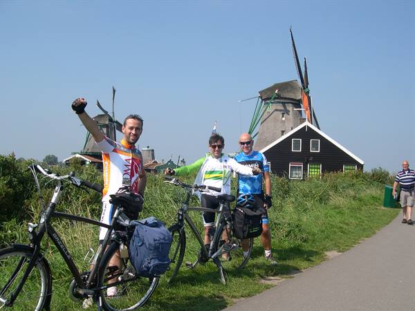 Cyclists with touring bikes beside Zaanse Schans windmills, black wooden house