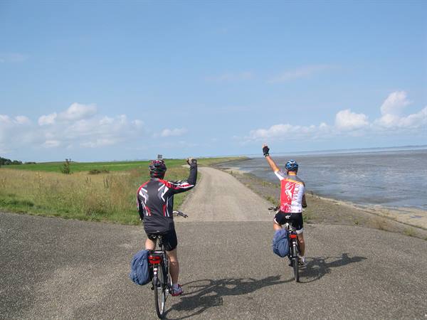 Two cyclists raise arms greeting on the dike beside shallow sea